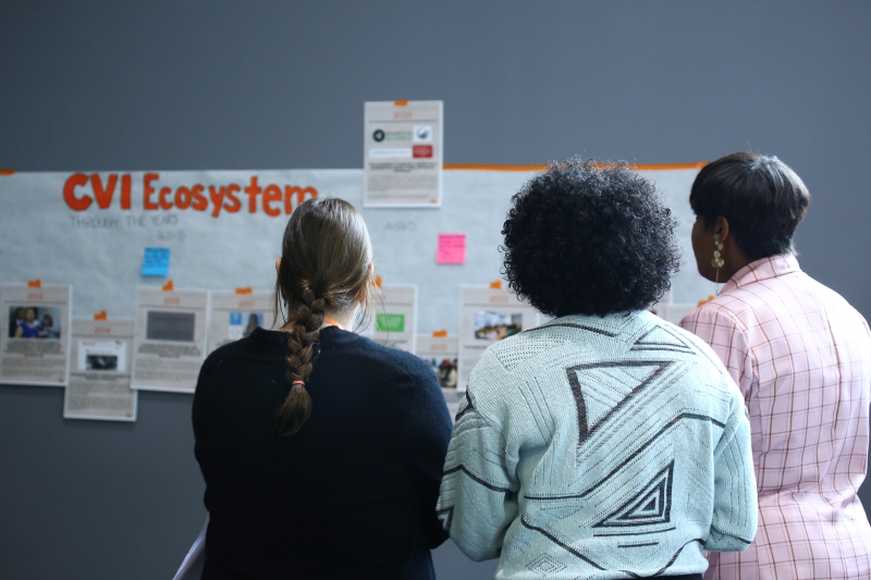 3 people looking at a bulletin board with several pages pinned to it